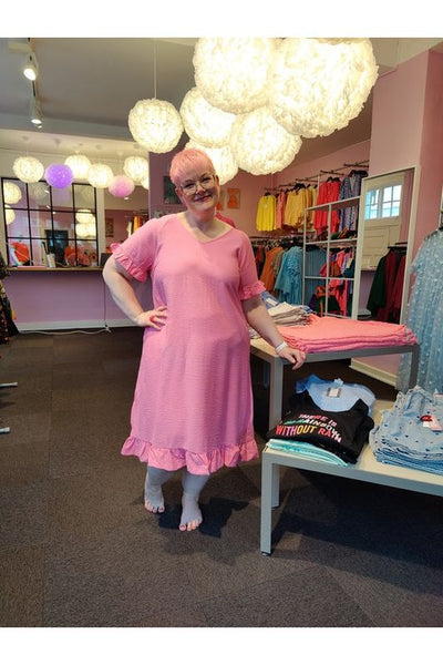 Billede af Heidi i en pink midikjole fra Simple Wish. Kjolen har korte ærmer, med flæsekant. I bunden af kjolen er der også en flæsekant.